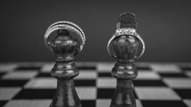 Chess pieces king and queen with jewelry rings on wooden chess board.