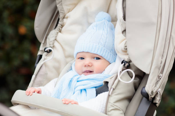 Baby boy in stroller. Child in pram in winter. Warm clothing for active walks with baby during cold season. Cute little kid in knitted hat and jacket sitting in pushchair. Infant in buggy.