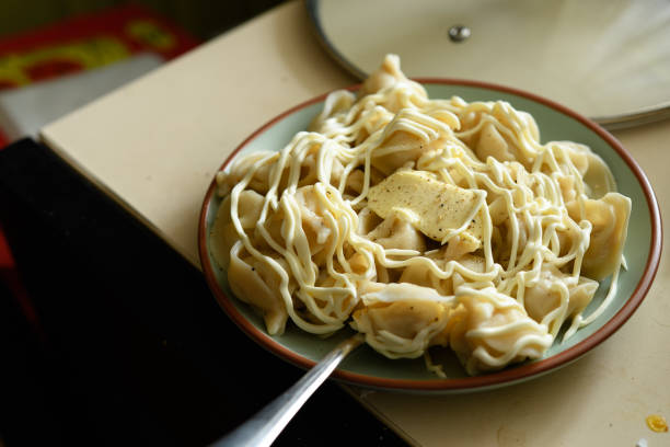 A portion of dumplings on a plate. Piece of butter melts. Seasoned dumplings with mayonnaise and pepper. Eating at home.