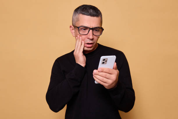 istock Shocked guy wearing glasses and jumper staring at smartphone feeling scared and sad while checking social media connected with technology standing indoor isolated over beige background 2177451810