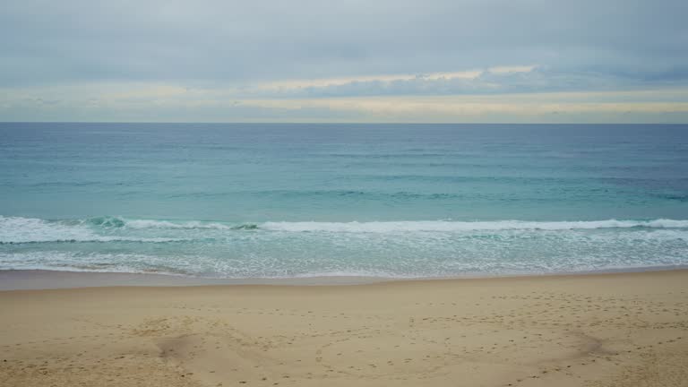 Wide shot empty beach with footprints on sand and small waves in ocean in winter