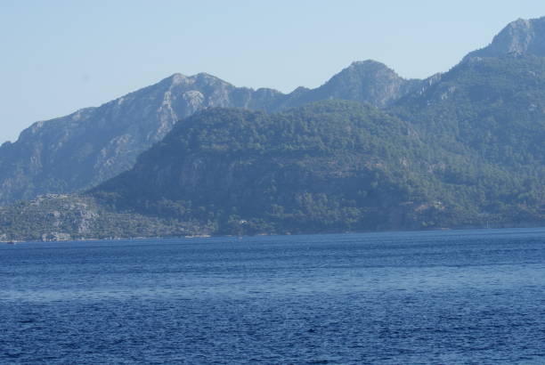 The photo shows the coast in Marmaris, Turkey, with azure sea, mountainous backdrop, and green forests.