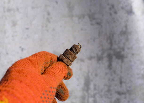 A hand in an orange glove holds a rusty spark plug