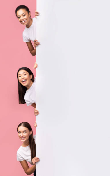 istock Three Girls Peeking Out Of Blank Board Posing, Pink Background 2177474471