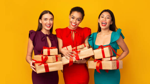 istock Three Models In Dresses Holding Wrapped Boxes Over Yellow Background 2177474820