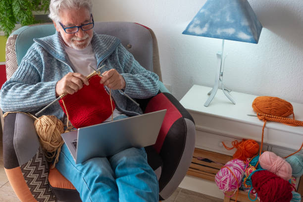 istock Senior man at home follows online knit tutorial to relax enjoying resting home leisure activity sitting on armchair - male people knitting with computer class help - people inner lifestyle hobby 2177476730