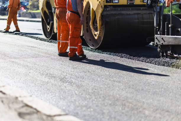 Road construction workers operating heavy machinery on a sunny day while laying asphalt on a new roadway