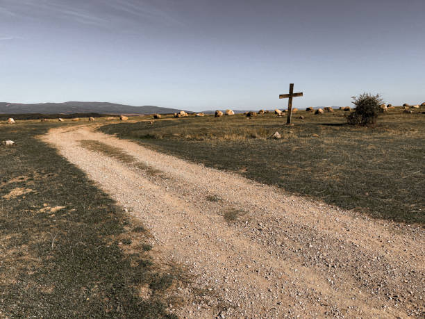 a cross showing a traveler’s path in a rural landscape and mountains in the background