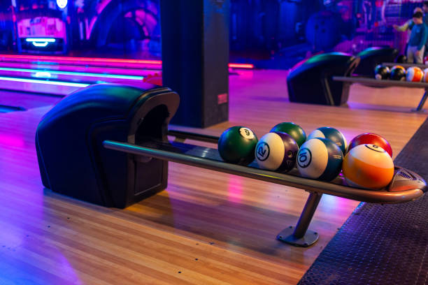 Various bowling balls arranged in stand on wooden lane at bowling hall Various bowling balls arranged in stand on wooden lane at bowling hall. Illuminated playroom in shopping center with no people bowling alley wood stock pictures, royalty-free photos & images