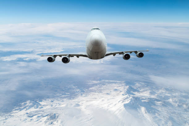 A large cargo airplane flying over snowcapped mountains.