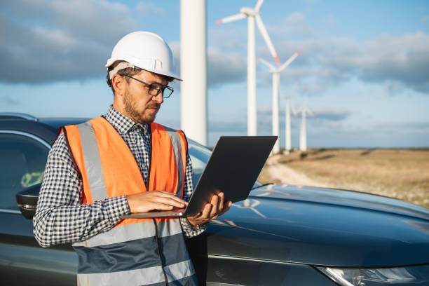 istock Technician standing in a field at a wind farm using laptop at sunset. 2177489323