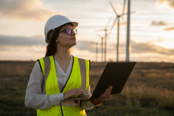 istock Female technician standing in a field at a wind farm using laptop at sunset. 2177489328
