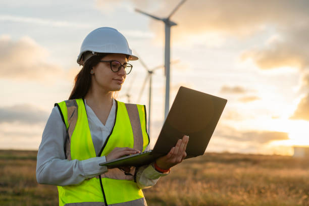 istock Female technician standing in a field at a wind farm using laptop at sunset. 2177489329