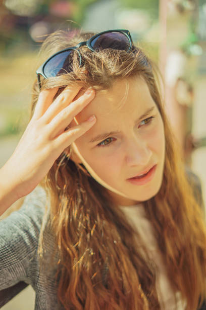 A young woman sits on the sun in city and clasps her head in her hands. Headache in a woman.