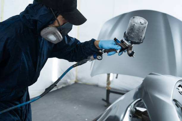 istock Car painter is changing the color of vehicle using sponge and paint sprayer. Worker is painting car in dark color with HVLP spray gun. 2177496573