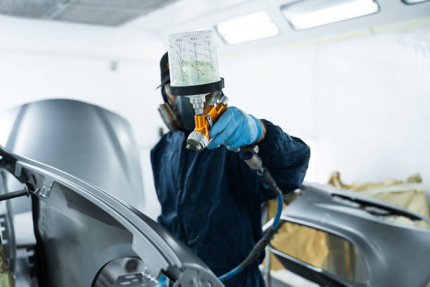 istock Car painter is finishing his paintwork on vehicle by applying lacquer with paint sprayer. Using LVLP spray gun to spread lacquer on metal. 2177496641