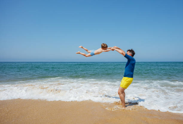 istock Joyful father spins son around as waves crash on a sunny beach 2177509297
