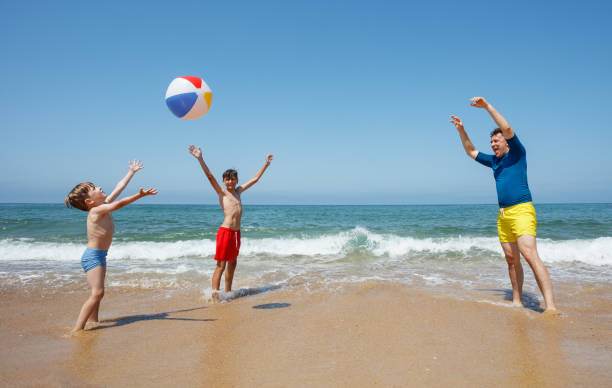 Man and young boys playfully pass beachball along the oceanfront