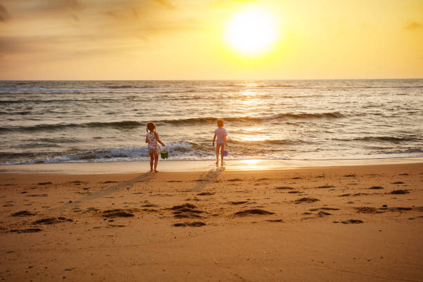 Two children, boy and girl walk along the sandy beach at sunset, their shadows stretching behind them, beautiful vacation time