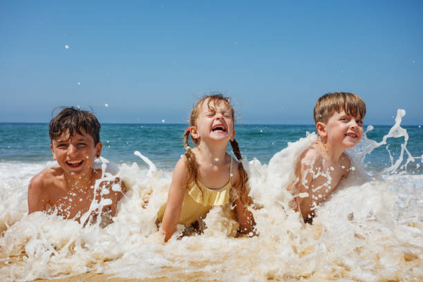 Two boys embrace the thrill of the waves crashing as they lay at the beach on summer vacations