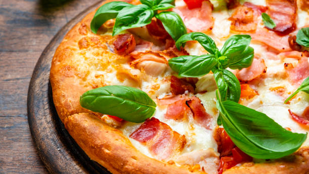 Small hot pizza with pancetta, mozzarella, tomato and basil on wooden background, top view