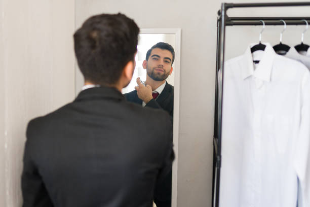 istock Man in business attire is applying cologne while checking his reflection in the walk-in closet mirror 2177511599