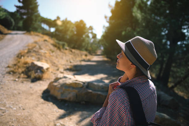A woman wearing a hat enjoys a peaceful, sunlit walk on a scenic nature trail, surrounded by trees and tranquility.