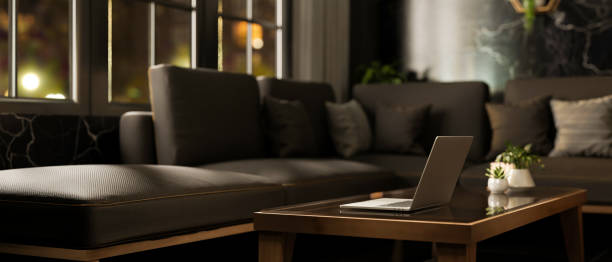 istock A laptop on a coffee table next to a large grey sofa in a modern black living room at night. 2177525577