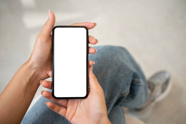 istock A woman in jeans sitting indoors and using her smartphone, with a white screen mockup displayed. 2177525597