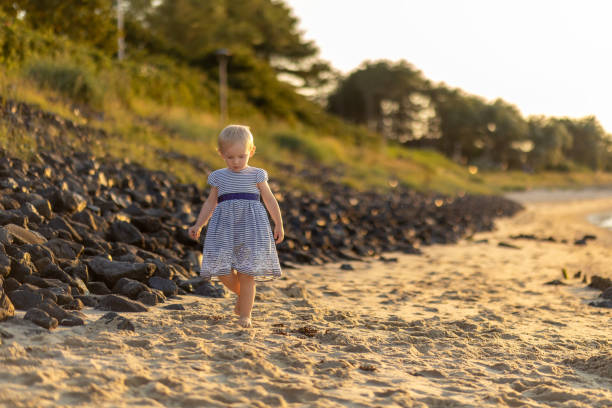 istock Little girl walking barefoot on a sandy beach at sunset 2177528606