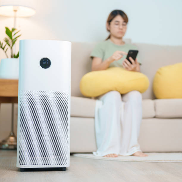 istock Air Purifier with woman relax and use smartphone on sofa. Purification system for filter and cleaning dust PM2.5 HEPA and virus in home. Allergy, Pure air, health, Wellness lifestyle and Air Pollution 2177533823