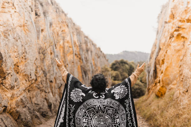 A Latina woman wearing a traditional poncho raises her arms to the sky in a rocky canyon landscape at Rocas de Suesca, Colombia