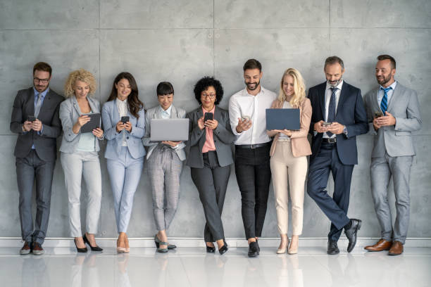 istock Business professionals aligned against a wall, engaged with digital devices. 2177550218