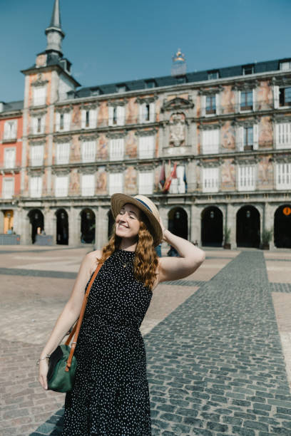 A woman basks in the warm sunlight at Plaza Mayor, one of Madrid’s most iconic squares. With its historic buildings as a backdrop, she smiles while adjusting her hat, capturing a moment of joy and appreciation for the city’s atmosphere.