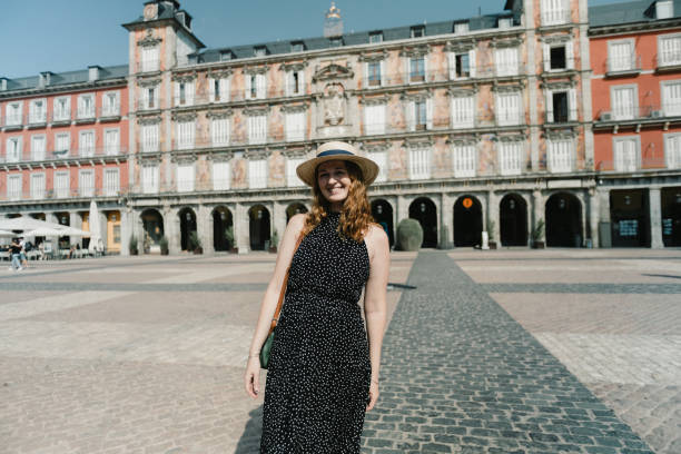 A woman basks in the warm sunlight at Plaza Mayor, one of Madrid’s most iconic squares. With its historic buildings as a backdrop, she smiles while adjusting her hat, capturing a moment of joy and appreciation for the city’s atmosphere.