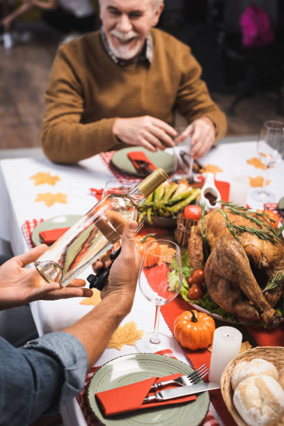 istock selective focus of man holding bottle of white wine while sitting at table served with thanksgiving dinner 2177555927