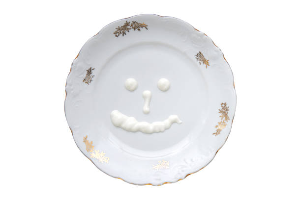 Porcelain plate with golden patterns on the edges isolated on white background and a smiley face made of sour cream inside