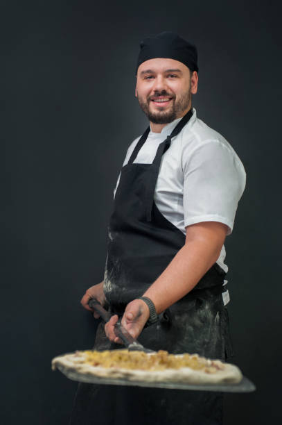 istock young, smiling, chef in a dark apron holding a spatula with a pizza blank before baking 2177558551