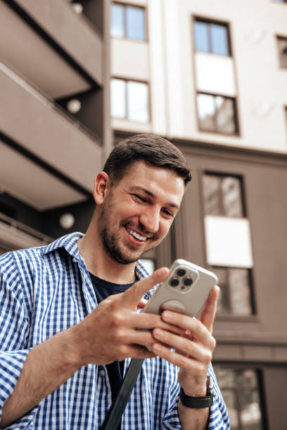 istock Young man happily using smartphone outside a modern building during daytime 2177558637