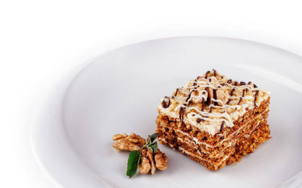 Slice of layered cake with walnuts and white chocolate drizzle, served on a white plate