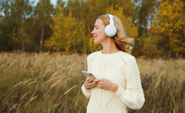 Happy inspired young woman enjoying listening to music in headphones with phone outdoors in autumn stock photo