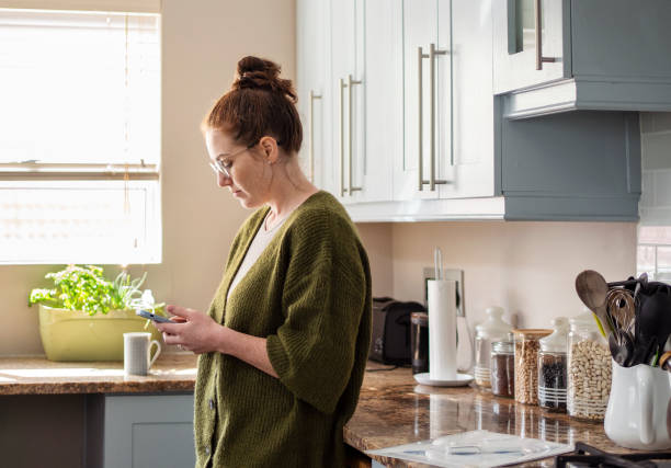 istock Young woman standing in her kitchen and texting on her phone 2177568480