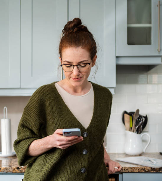 istock Young woman standing in her kitchen and smiling at a phone message 2177568526
