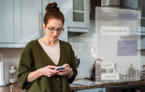 istock Young woman chatting online on her phone while standing in her kitchen 2177568541