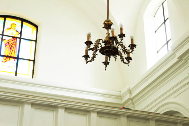 A ceiling lamp with candles hangs in a church on a white light background. Interior of religious buildings.