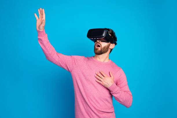 Young man wearing virtual reality headset, expressing awe and excitement. Immersive VR experience on vivid blue backdrop.