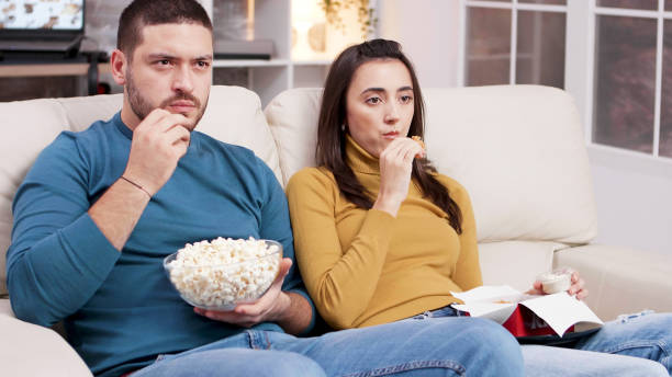 istock Couple sitting on couch eating fried chicken 2177581246