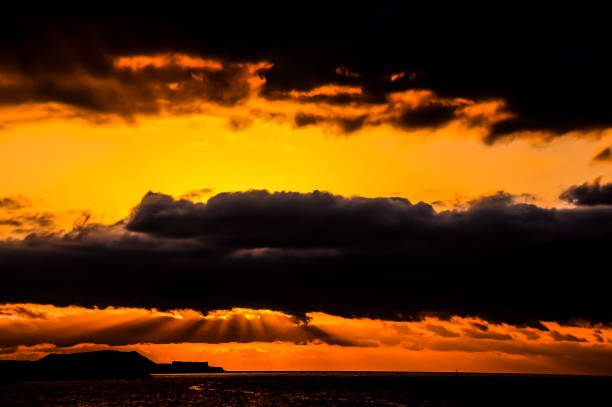 The sky is dark and cloudy with a beautiful orange sunset. The clouds are low and the sun is setting, creating a serene and peaceful atmosphere