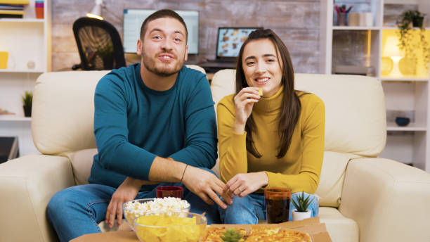 istock Couple sitting on couch laughing while watching tv and eating pizza 2177582694