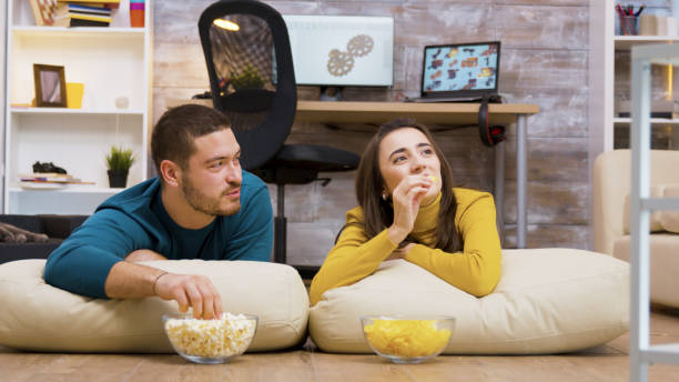 istock Cheerful couple watching tv sitting on pillows 2177582729